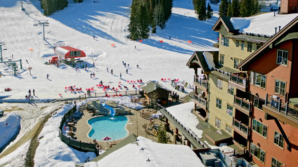 A lively exterior scene showcasing the ski slopes, a sparkling swimming pool, the ski lift, and the lodge’s inviting architecture. Snow blankets the area, and the juxtaposition of the pool and slope highlights diverse resort amenities.