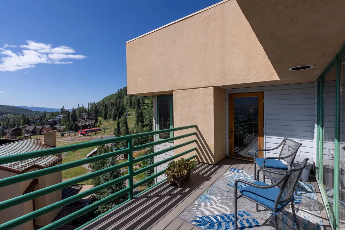 A private balcony with blue chairs, a decorative rug, and a railing overlooking majestic mountain views. The peaceful setting invites guests to relax, enjoy a coffee, or take in the sunset from their own retreat.