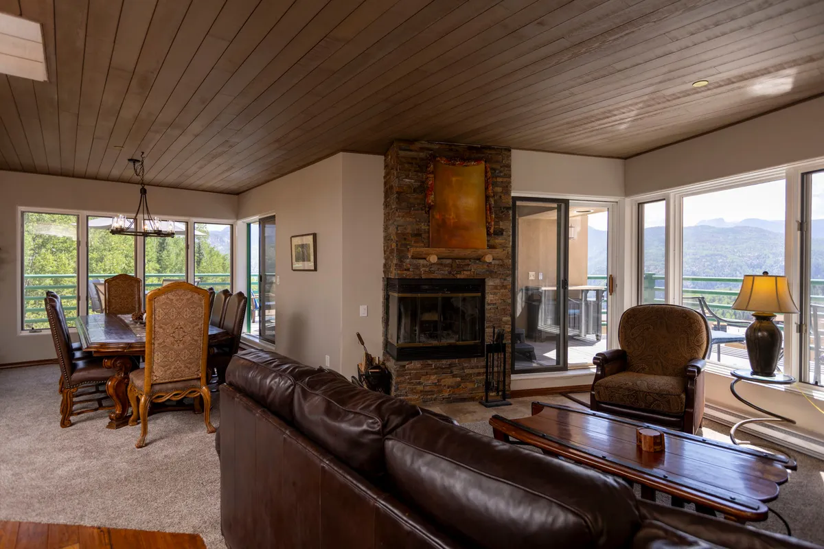 An inviting open-plan living and dining area with a glowing fireplace, large windows revealing sunset mountain views, and a dining table set for gatherings. The space radiates warmth and togetherness, ideal for both quiet evenings and lively group meals.