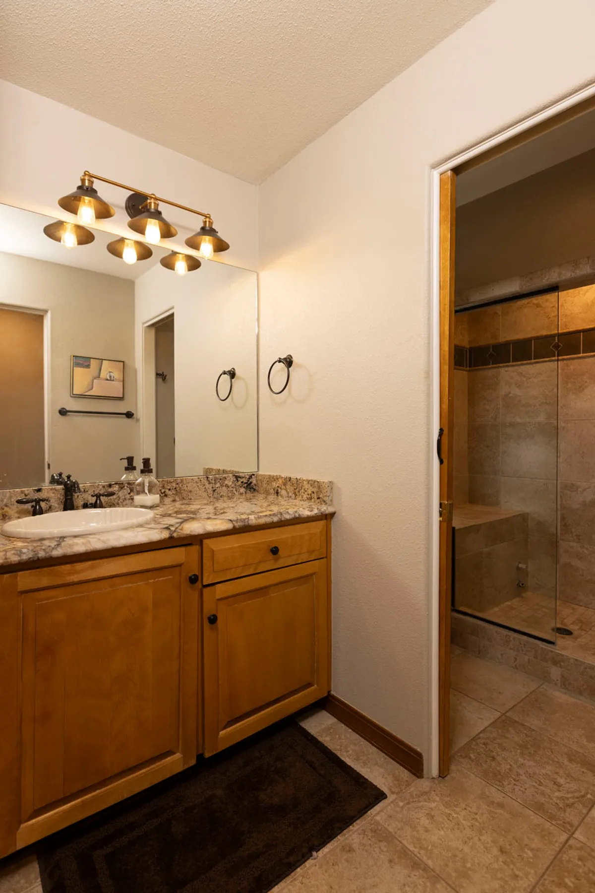 A modern bathroom featuring a granite countertop, stylish light fixtures, a large mirror, and a spacious shower area. The space is inviting, functional, and ideal for both relaxation and daily routines.