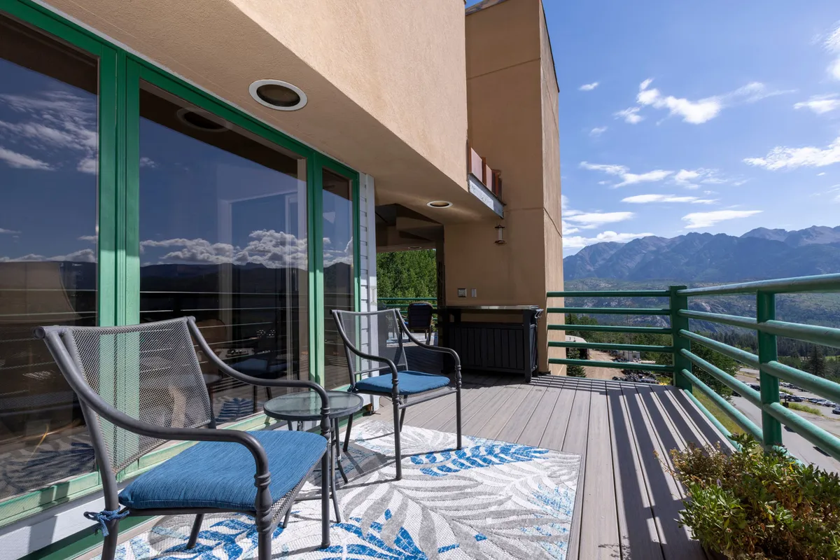 An outdoor seating area with comfortable chairs, a decorative rug, and a backdrop of vibrant mountain vistas. The green railings and cozy arrangement invite groups to relax, socialize, or stargaze together in a peaceful mountain setting.
