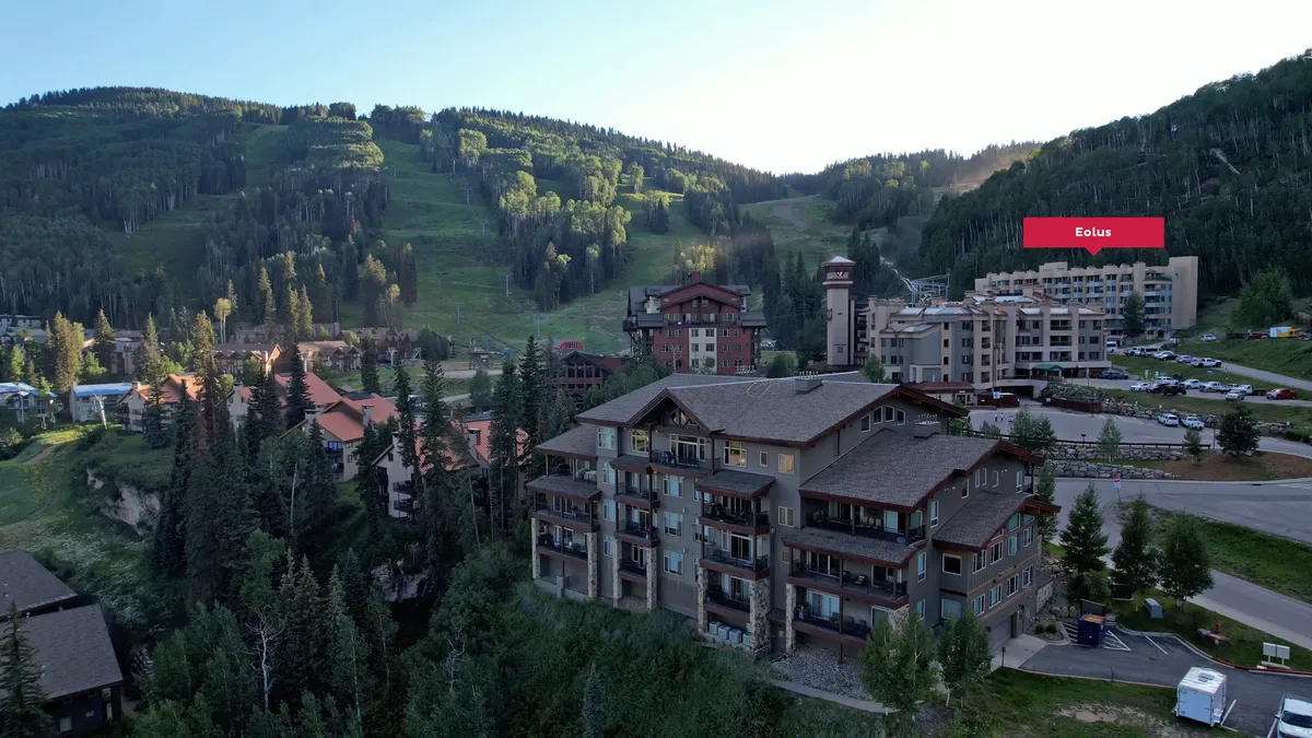 An expansive mountain landscape with resort buildings nestled among green trees at the base, hinting at year-round outdoor adventure. The scene balances natural beauty with the welcoming structures of Purgatory Resort.