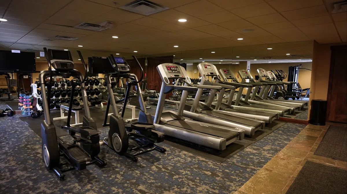 A modern, well-equipped fitness center with treadmills, ellipticals, dumbbells, and expansive mirrors. The bright, clean space is designed for both individual workouts and group fitness activities, and feels uplifting and energetic.