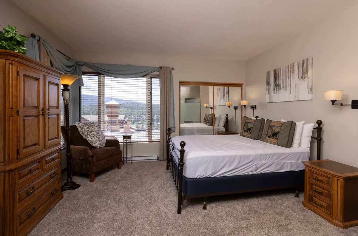This image features a serene bedroom with a queen-sized bed, wooden wardrobe, a comfortable armchair, and a large window offering a beautiful mountain view. The space feels cozy and peaceful, perfect for restful nights.
